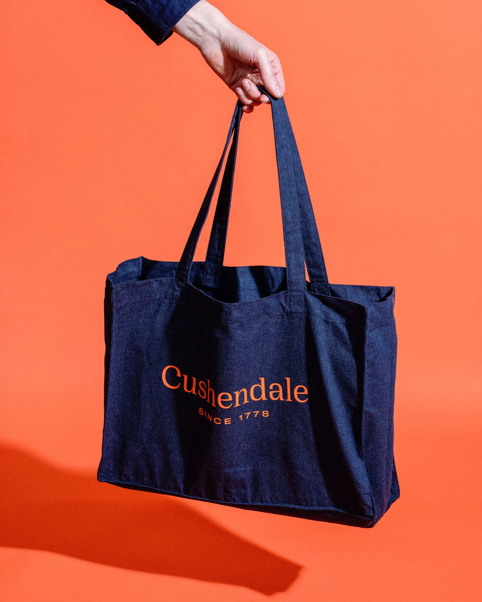 Hand holding navy canvas Cushendale bag against a bright orange backdrop