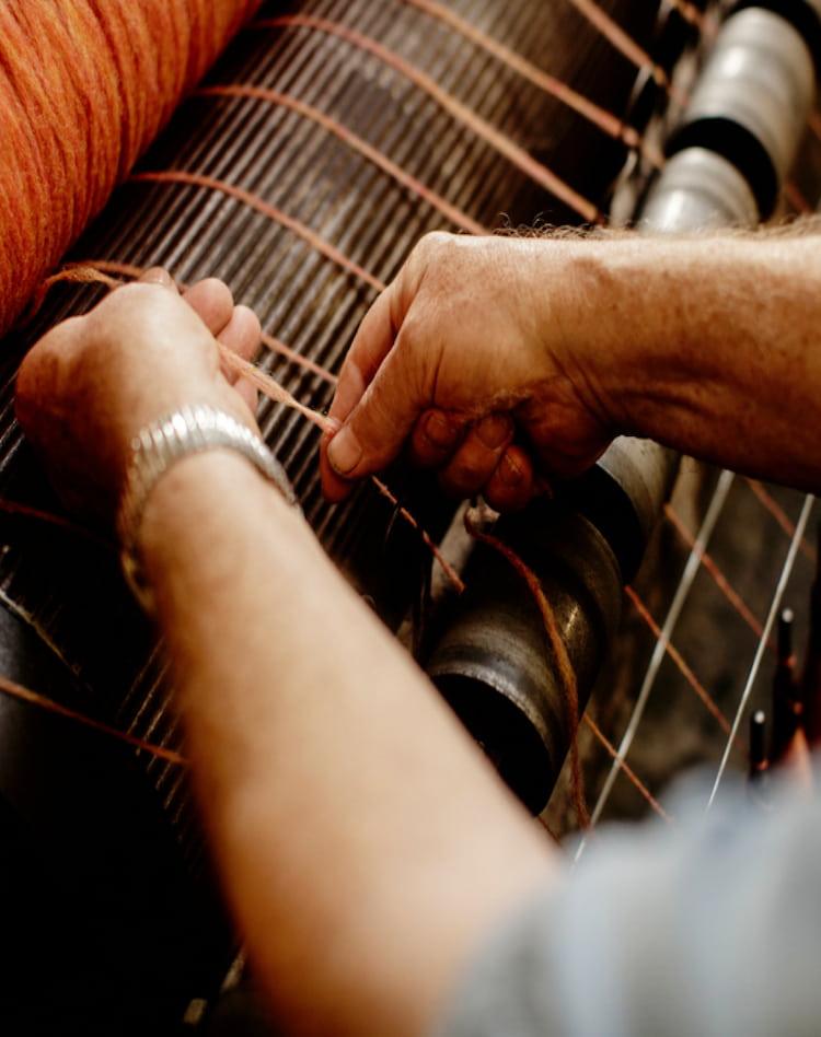 Hands pulling orange wool threads on a loom