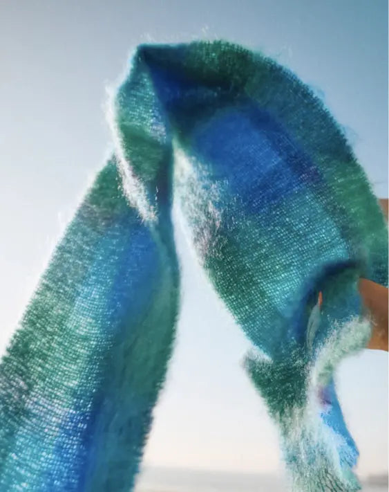 Blue and green tartan scarf flowing through the air against a light blue sky 