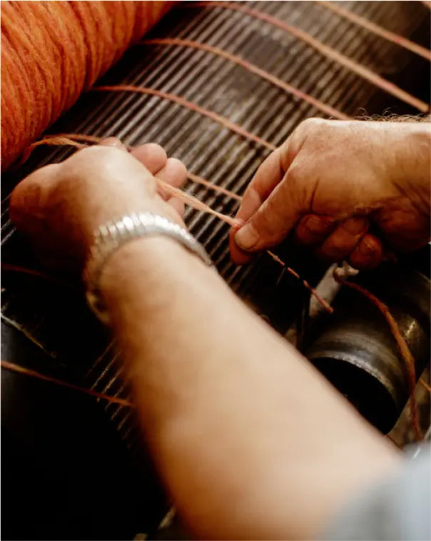 Hands pulling orange wool threads on a loom