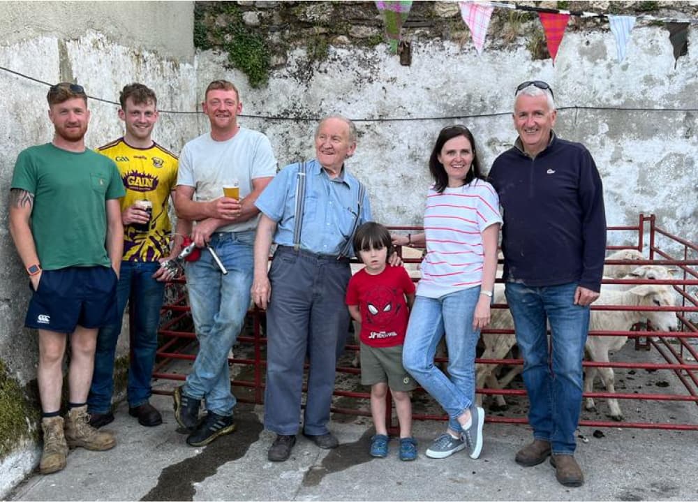 Members of the Cushen family with Paddy outdoors in front of a small pen of sheep