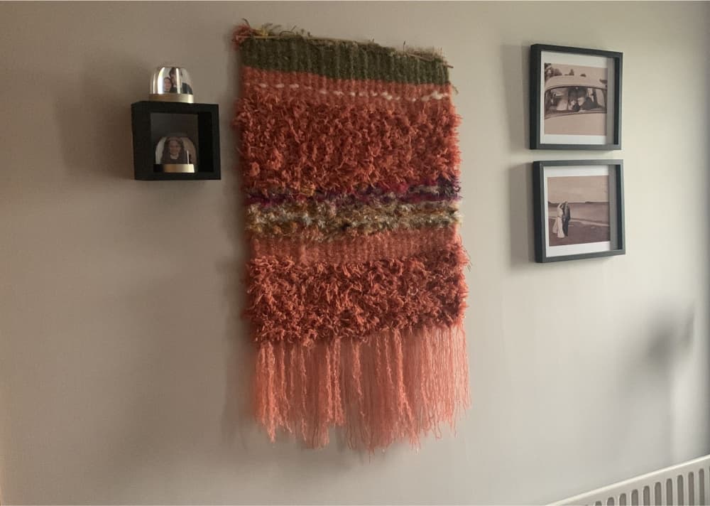 Repurposed orange wall hanging made from fibre selvedge and yarn ends hanging on the wall in a family home
