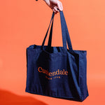 Hand holding navy canvas Cushendale bag against a bright orange backdrop