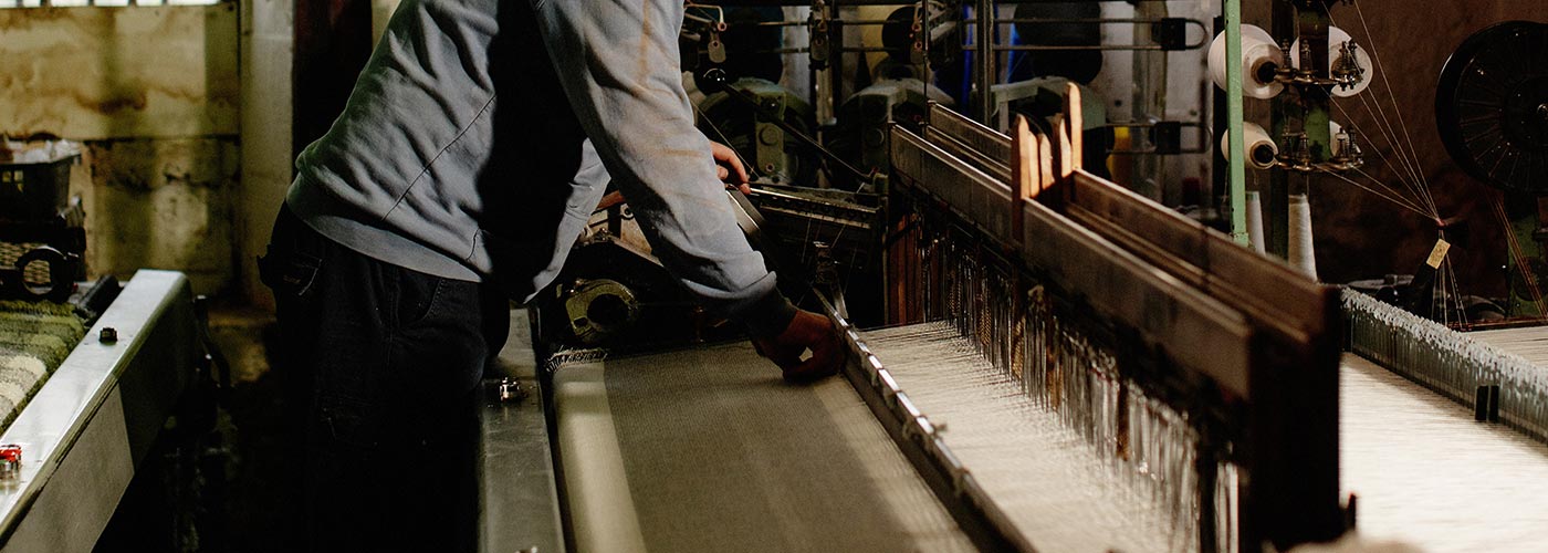 A person operating a machine to weave wool threads in the workshop