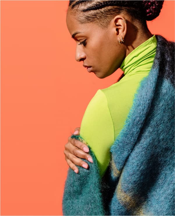 Woman wrapped in a teal blue woollen blanket looking down to the left against a bright orange backdrop 