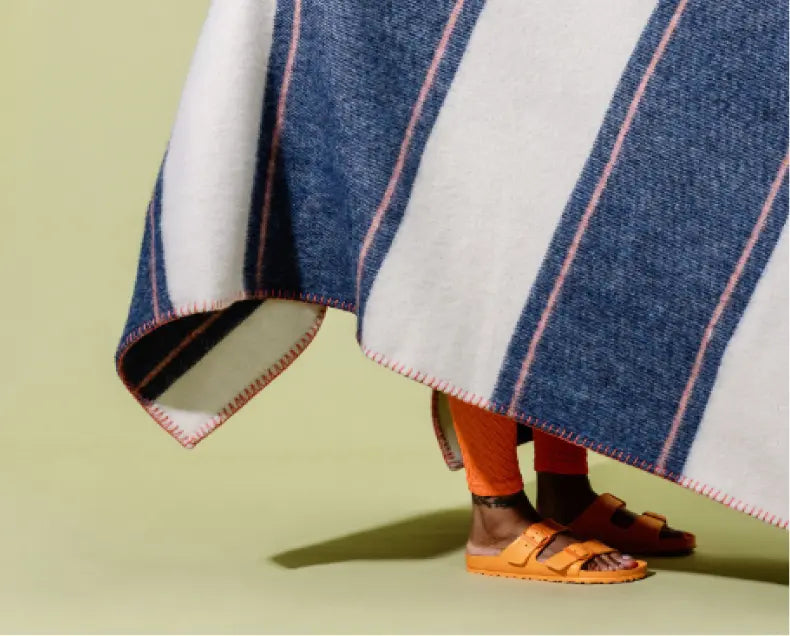 large navy and white striped bed blanket covering a person showing only their ankles and orange sandals