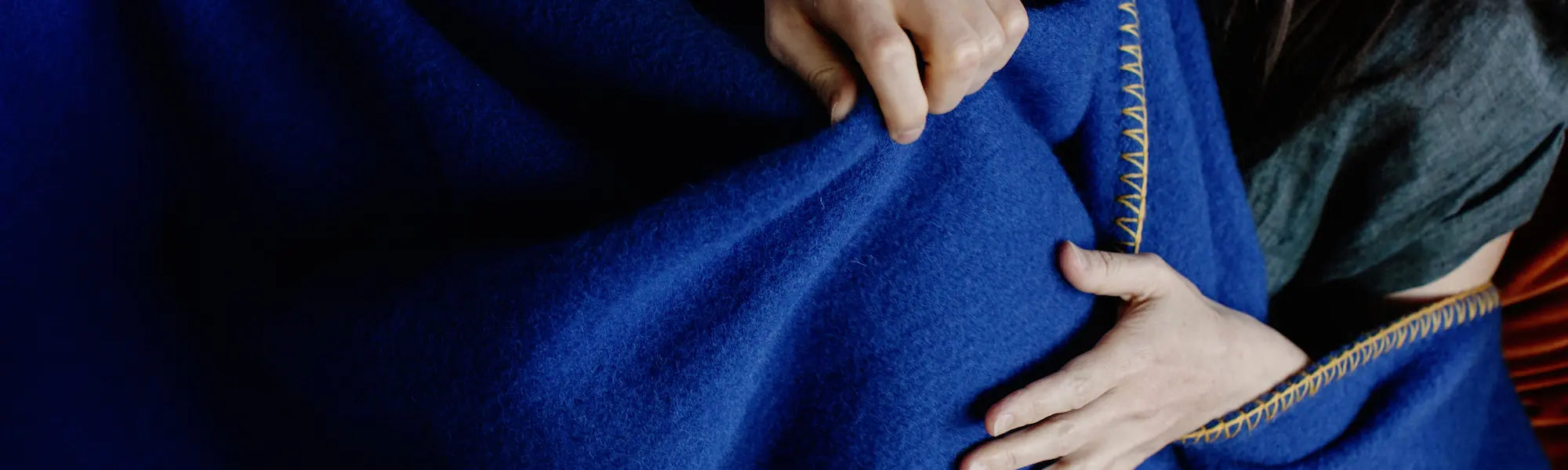 Hands feeling and pulling a deep blue throw blanket