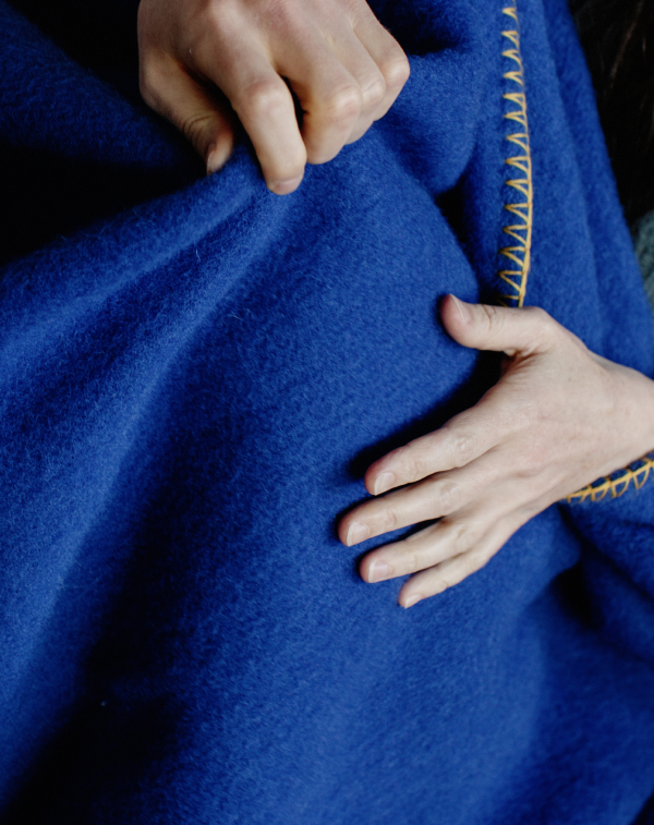Close up shot of hands feeling and pulling a deep blue throw blanket