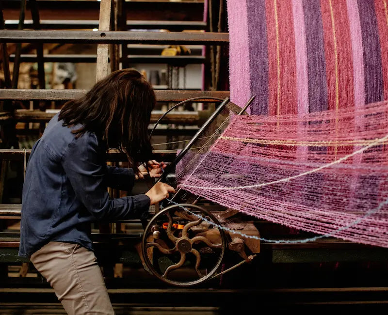 Miriam Cushen using a warping technique on a loom with pink, red and purple threads at the mill