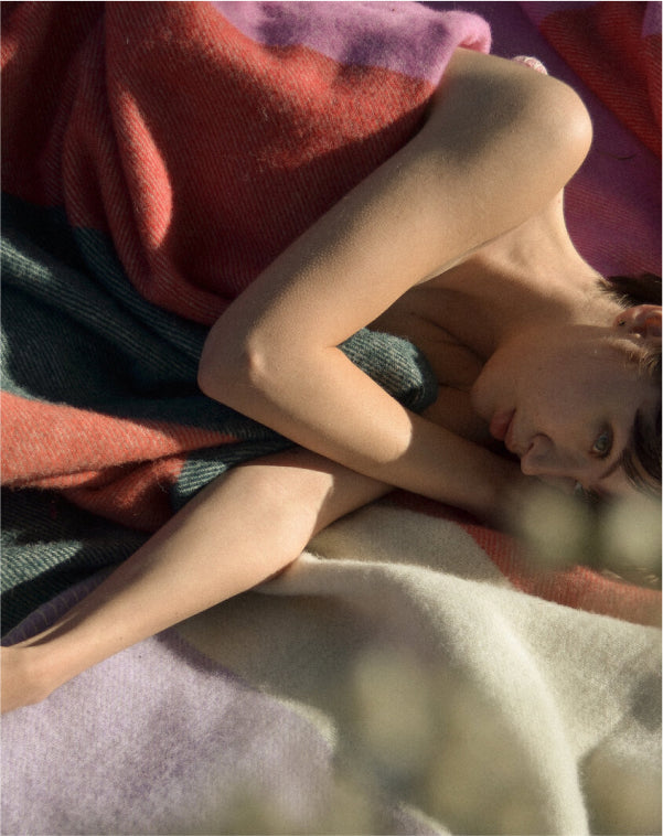 Woman lying on her side outside wrapped in “Touch” blanket by MC Kirwan and Cushendale