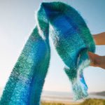Blue and green tartan scarf flowing through the air against a light blue sky and sandy beach background