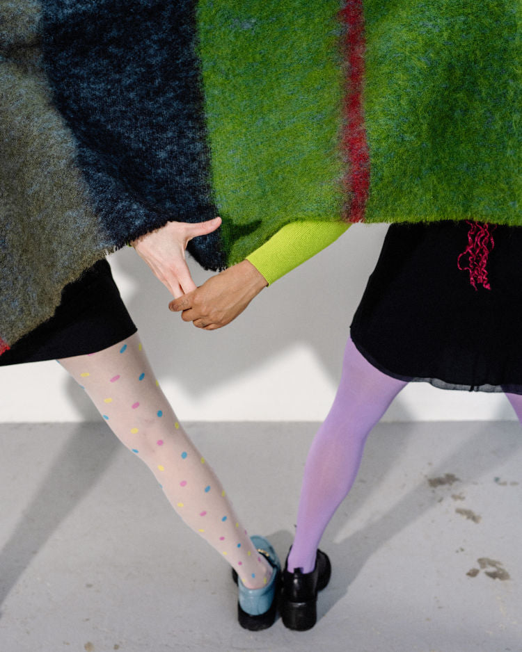 Dancers in colourful tights and covered from the waist up in a navy and green plaid blanket hold hands