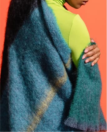 A large teal blue and green woollen blanket wrapped around a woman's back and shoulders