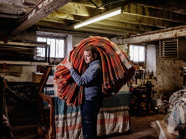 Portrait of Thomas hauling fabric over his shoulder at the mill